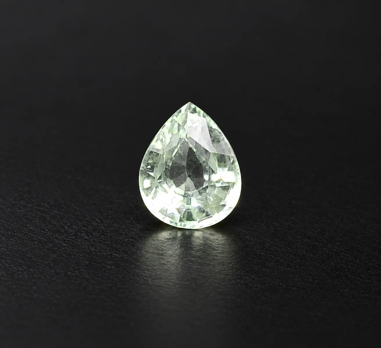 A pale green pear-shaped gemstone glowing against a black background